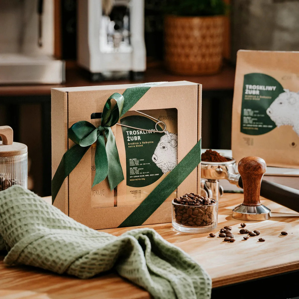 Pudełko prezentowe CRAFTBE z zieloną wstążką i Troskliwym Żubrem 250 g, obok słój ziaren i tamper